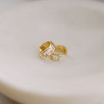 Two gold earrings with small designs on a beige surface