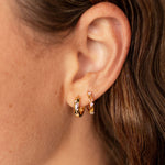 Load image into Gallery viewer, Close-up of a person wearing gold hoop earrings with a blurred background
