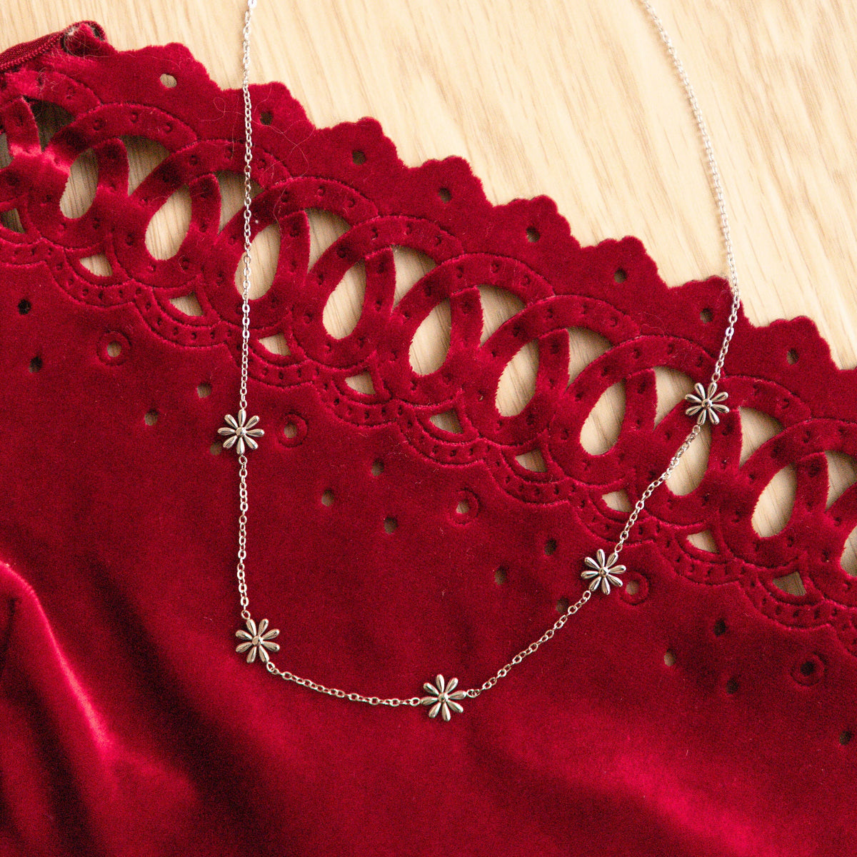 Silver necklace with floral pendants on a red lace garment against a wooden background