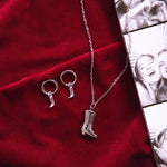 Load image into Gallery viewer, Silver necklace with cowboy boot and earring pendants on a red fabric background
