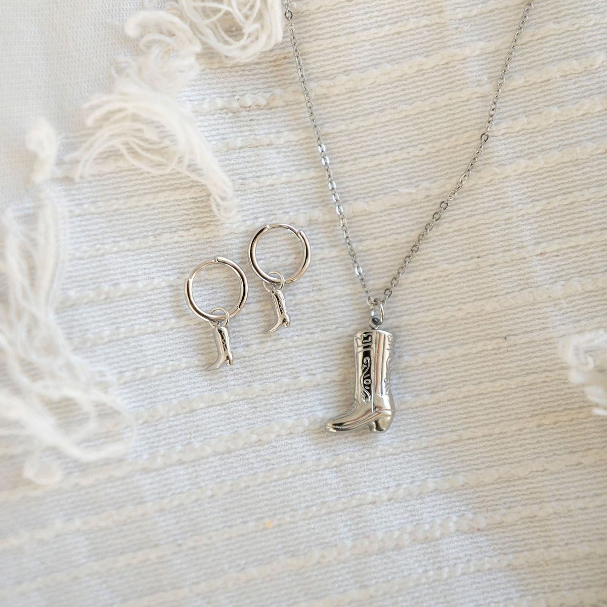 Silver boot hoops and boot necklace on white fabric background