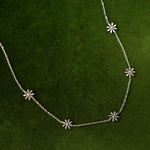 Load image into Gallery viewer, Silver necklace with flower shaped pendants on a green background
