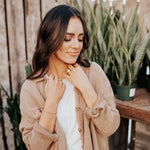 Woman adjusting her necklace outdoors with plants in the background
