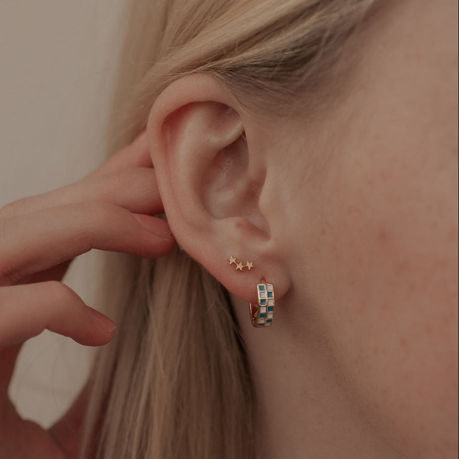Close-up of an ear with small star earrings and a hand adjusting hair.