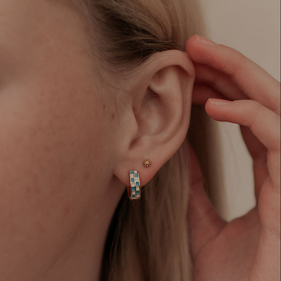 Close-up of a person wearing a small hoop earring and sunshine flat back stud with a hand adjusting it.