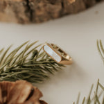 Load image into Gallery viewer, Gold ring with a white stone on a wooden surface with pine branches
