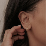 Close-up of a person adjusting an earring with a neutral background