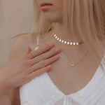Woman wearing a white top with delicate necklaces against a neutral background