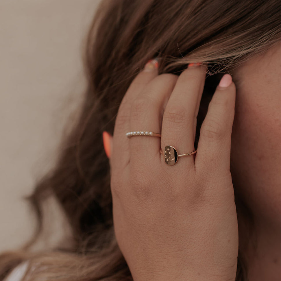 Close-up of a hand with gold rings and a bracelet, holding hair against a neutral background