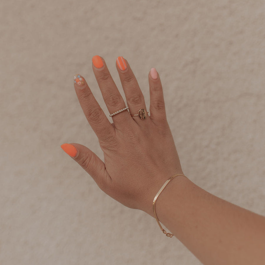 Hand with orange nail polish and gold rings on a beige background