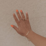 Load image into Gallery viewer, Hand with orange nail polish and gold rings on a beige background
