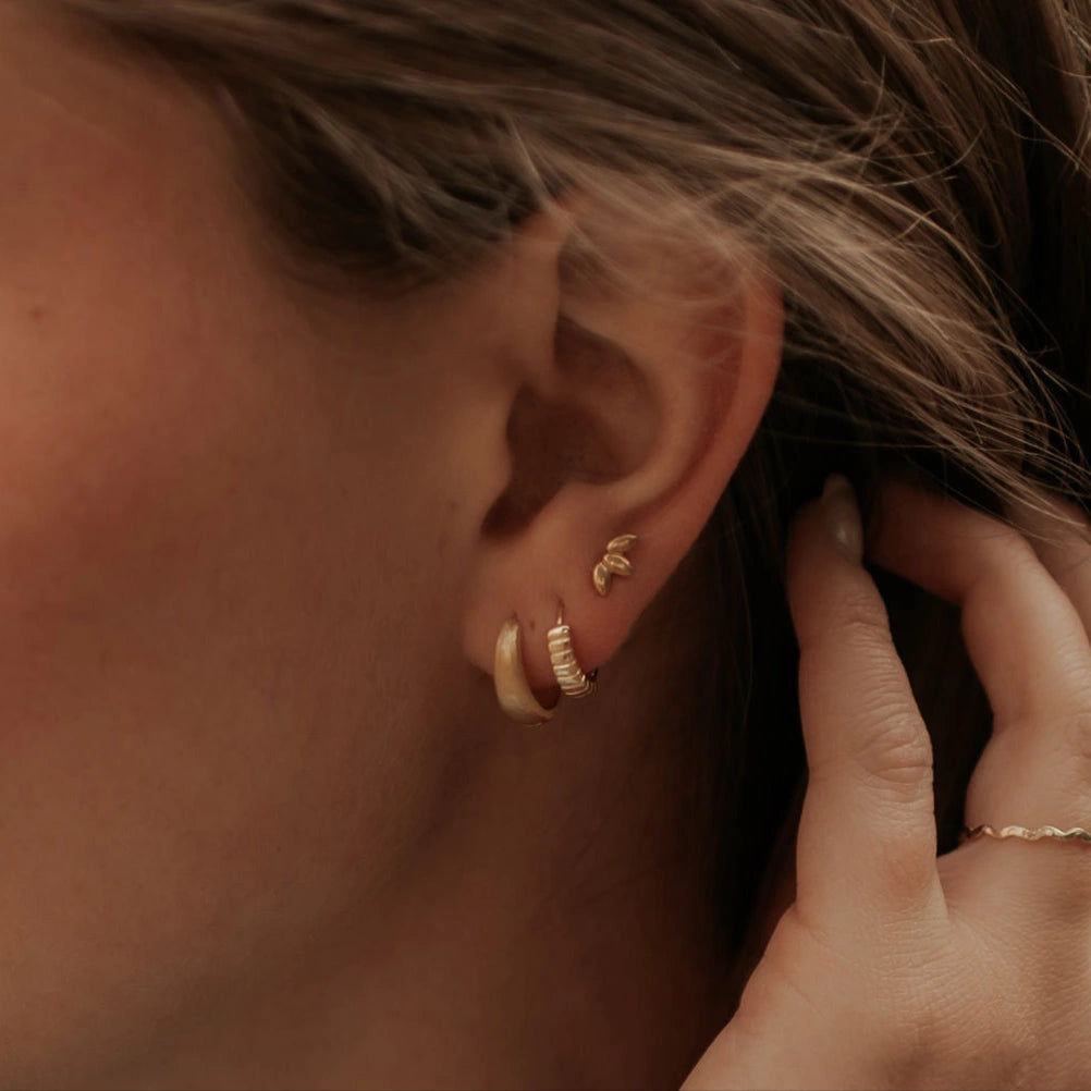 Close-up of an ear with gold hoop earrings and a hand adjusting them.