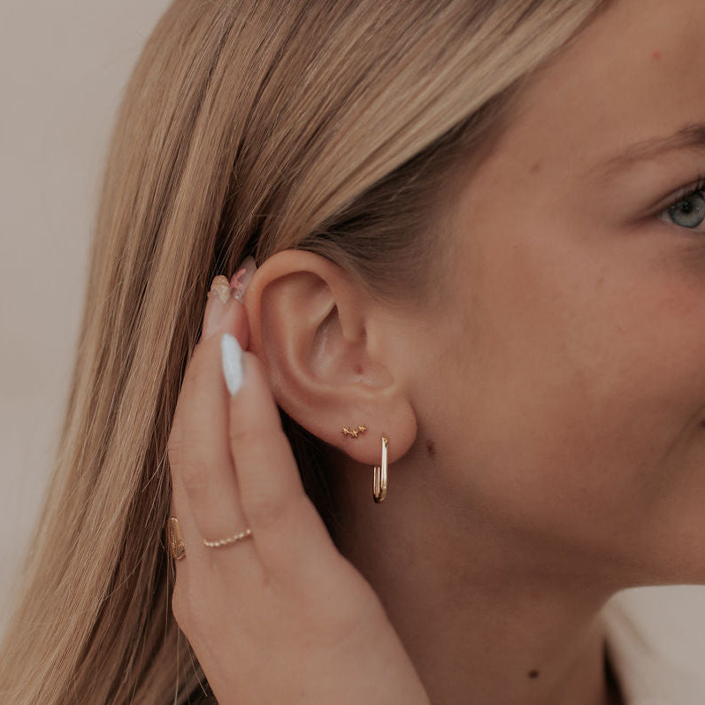 Woman wearing gold earrings and a bracelet, with a neutral background