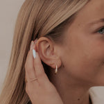 Woman wearing gold earrings and a bracelet, with a neutral background
