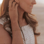 Woman adjusting an earring on a blurred beach background