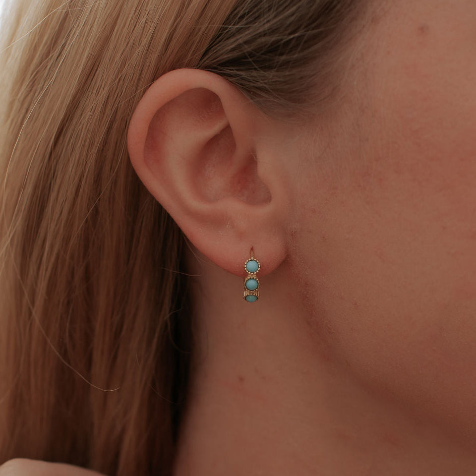 Close-up of an ear wearing turquoise earrings with a blurred background