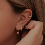 Close-up of a person wearing gold earrings with floral designs.