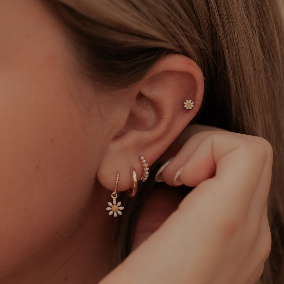 Close-up of a person wearing gold earrings with floral designs.