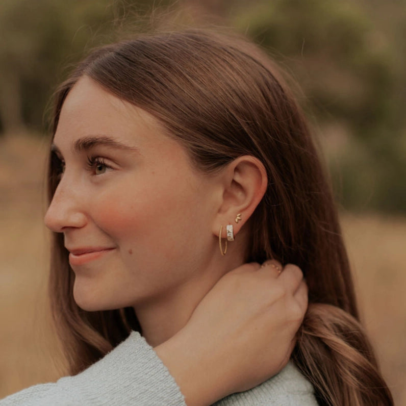Woman adjusting her hoop earring outdoors with a blurred natural background