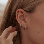 Close-up of a person's ear with earrings and hair in a blurred outdoor setting