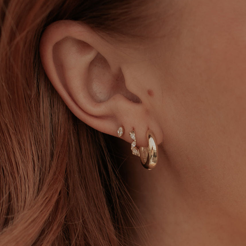Close-up of an ear with gold hoop earrings against a blurred background