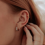 Close-up of a person wearing a gold earring with a blurred background