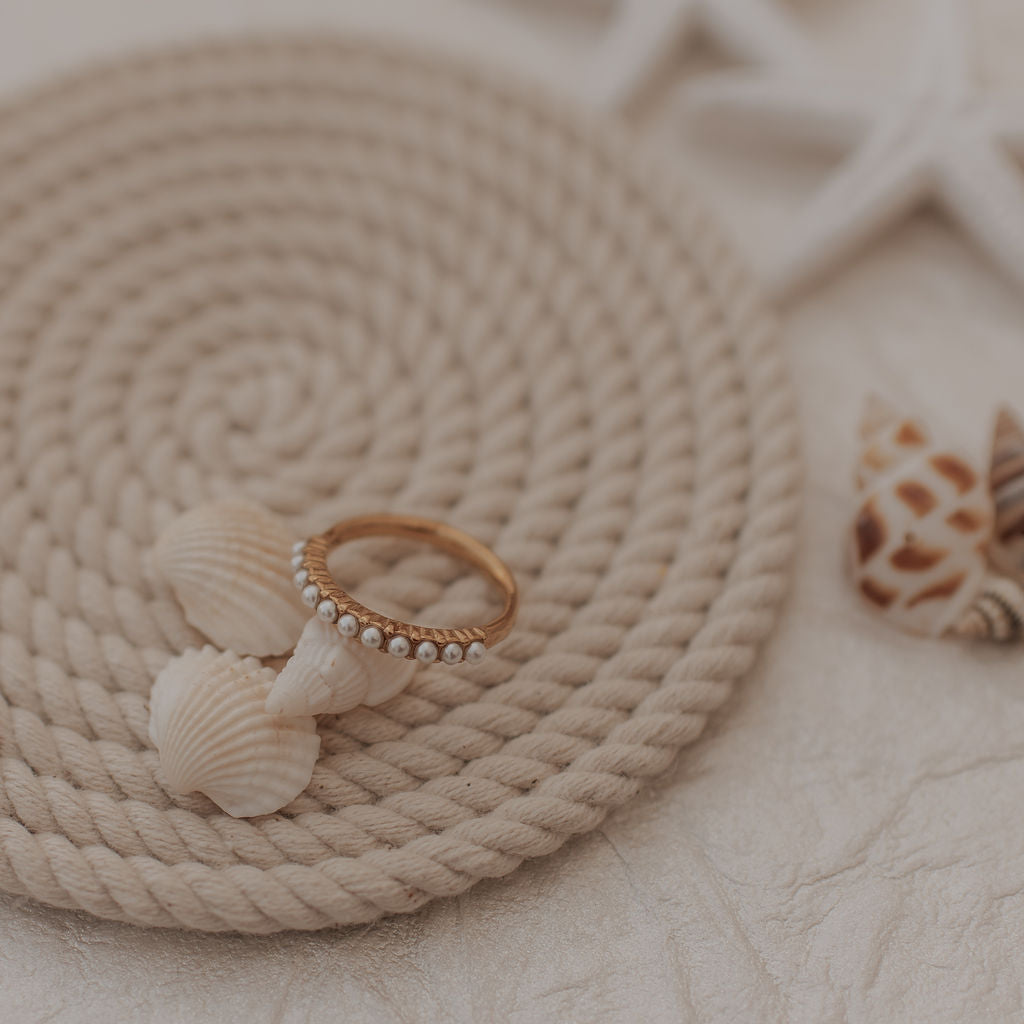 Ring with pearl details on a rope mat with starfish and shell decorations.