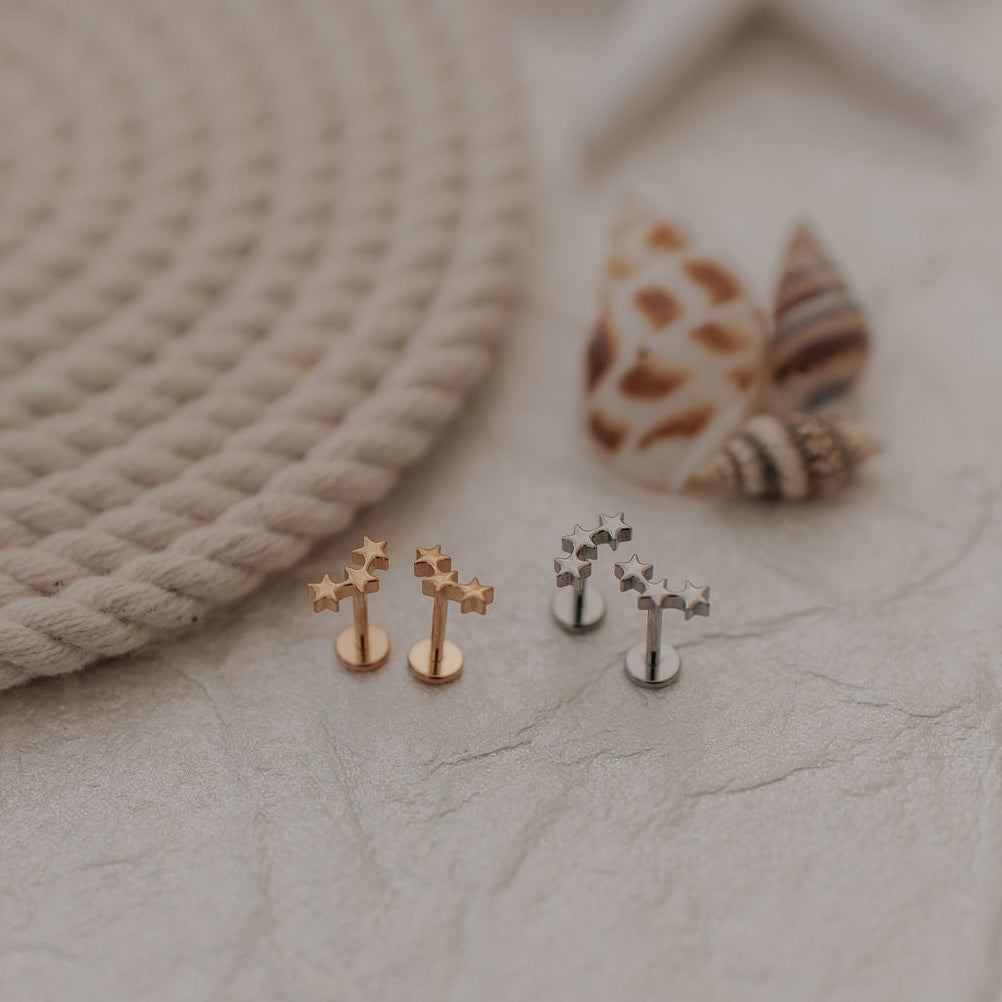 Set of small earrings on a textured surface with rope and shells in the background