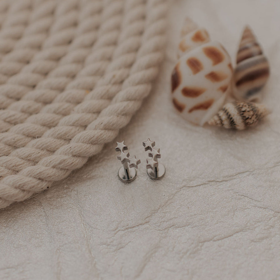 Pair of silver star earrings on a textured surface with a rope and shell in the background.