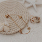 Gold bracelet with floral designs on a textured surface with shells and starfish.