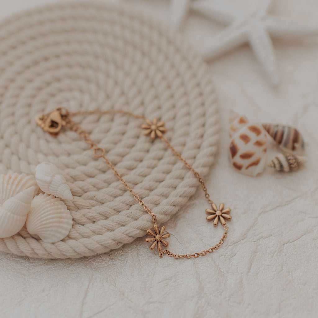 Gold bracelet with floral designs on a textured surface with shells and starfish.