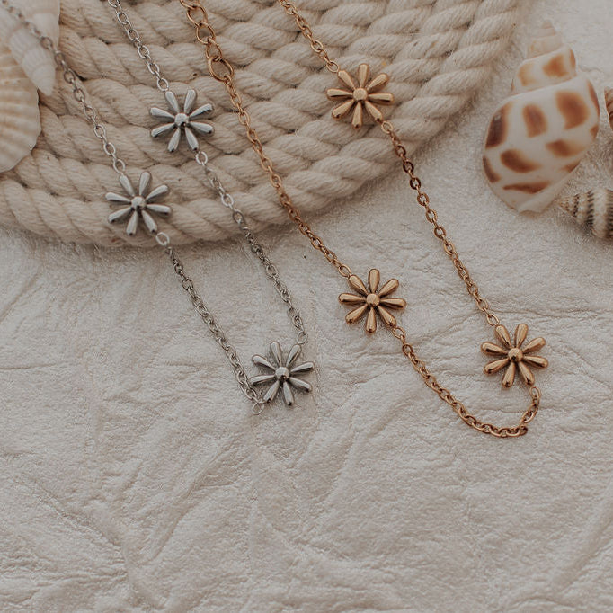 Two bracelets with flower-shaped pendants on a textured surface with seashells.