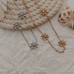 Load image into Gallery viewer, Two bracelets with flower-shaped pendants on a textured surface with seashells.

