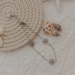 Silver flower-shaped earring on a textured surface with rope and shells