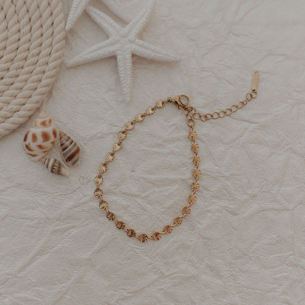 Gold bracelet on a textured beige surface with starfish and rope