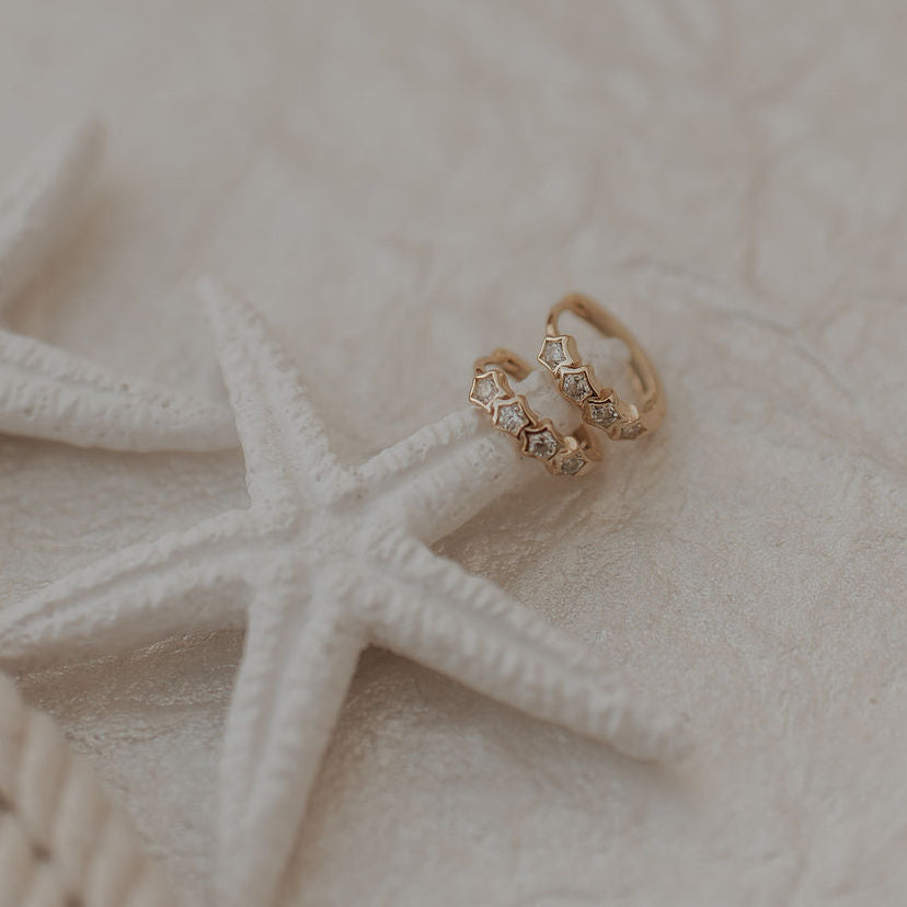 Gold star earrings on a starfish with a textured beige background