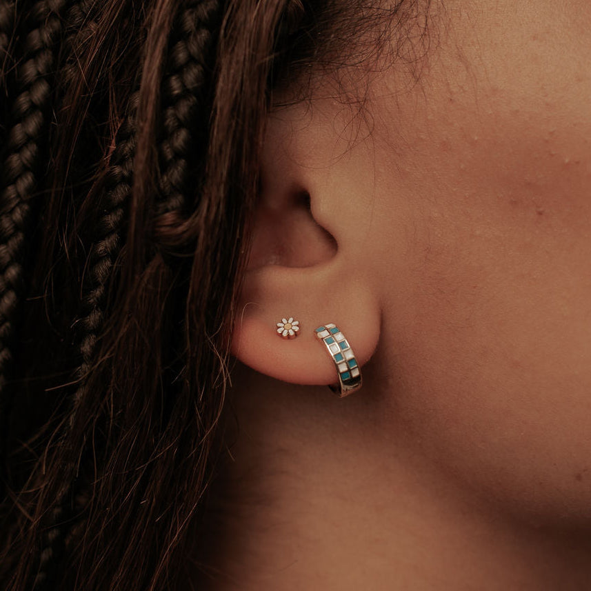 Close-up of an ear with daisy flat back earrings and blue and white checkered hoops and braided hair
