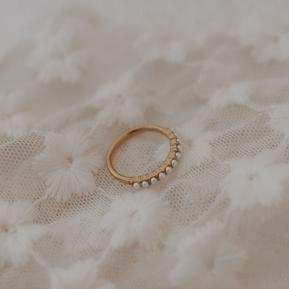 Gold ring with small pearls on a textured beige fabric background