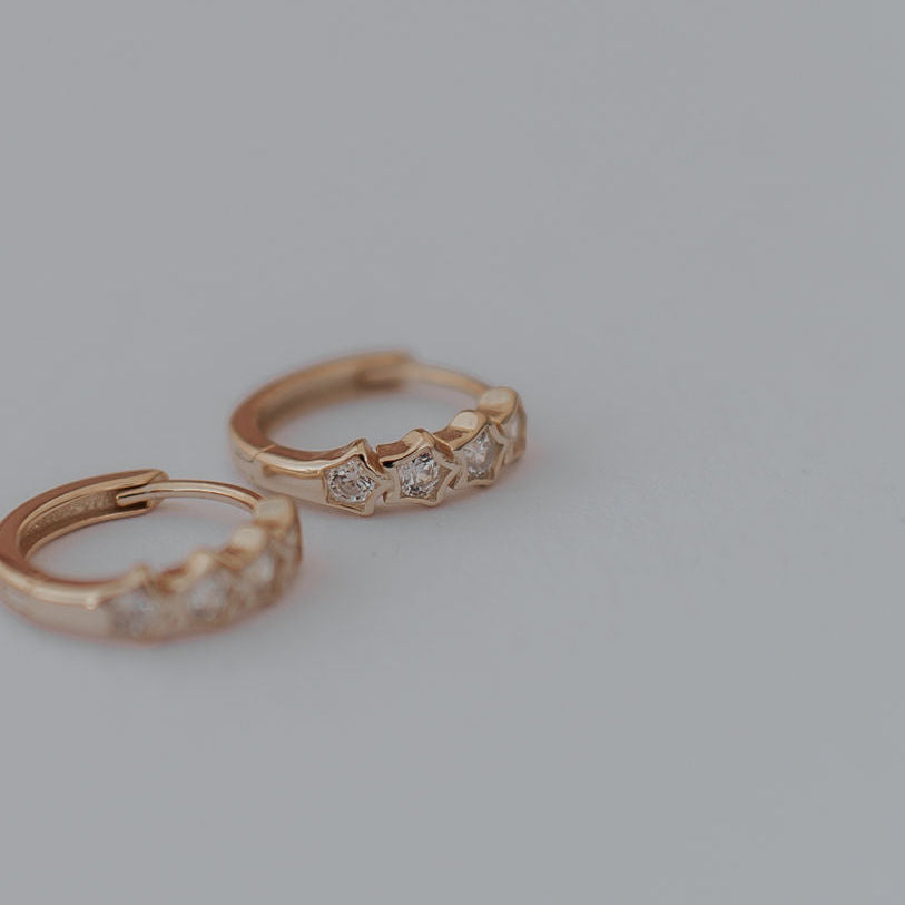 Pair of gold hoop star earrings with small diamonds on a light gray background