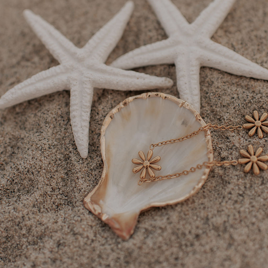 Gold bracelet with floral pendants on a shell and starfish on sand