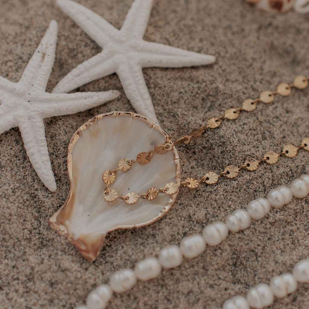 Pearl necklace and gold chain on sand with starfish and shells