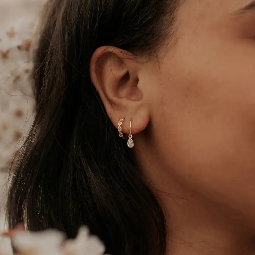 Close-up of an ear wearing a gold earring with a blurred background