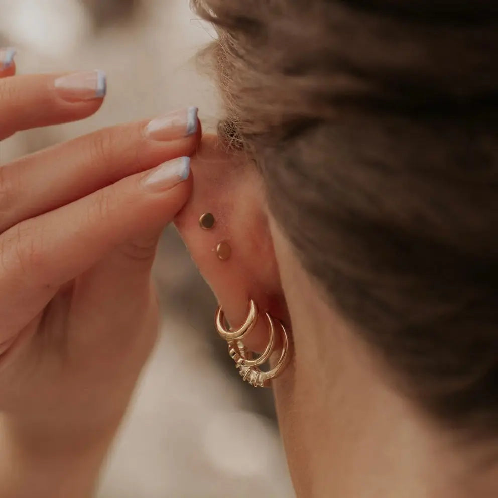 Close-up of a person wearing gold hoop earrings and flat back studs with a blurred background