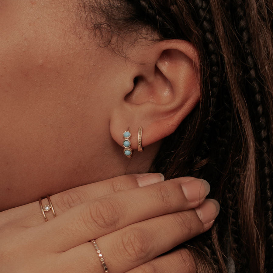Close-up of an ear with earrings and a hand wearing rings, with a blurred background.