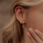 Load image into Gallery viewer, Close-up of a person wearing gold earrings with a blurred background
