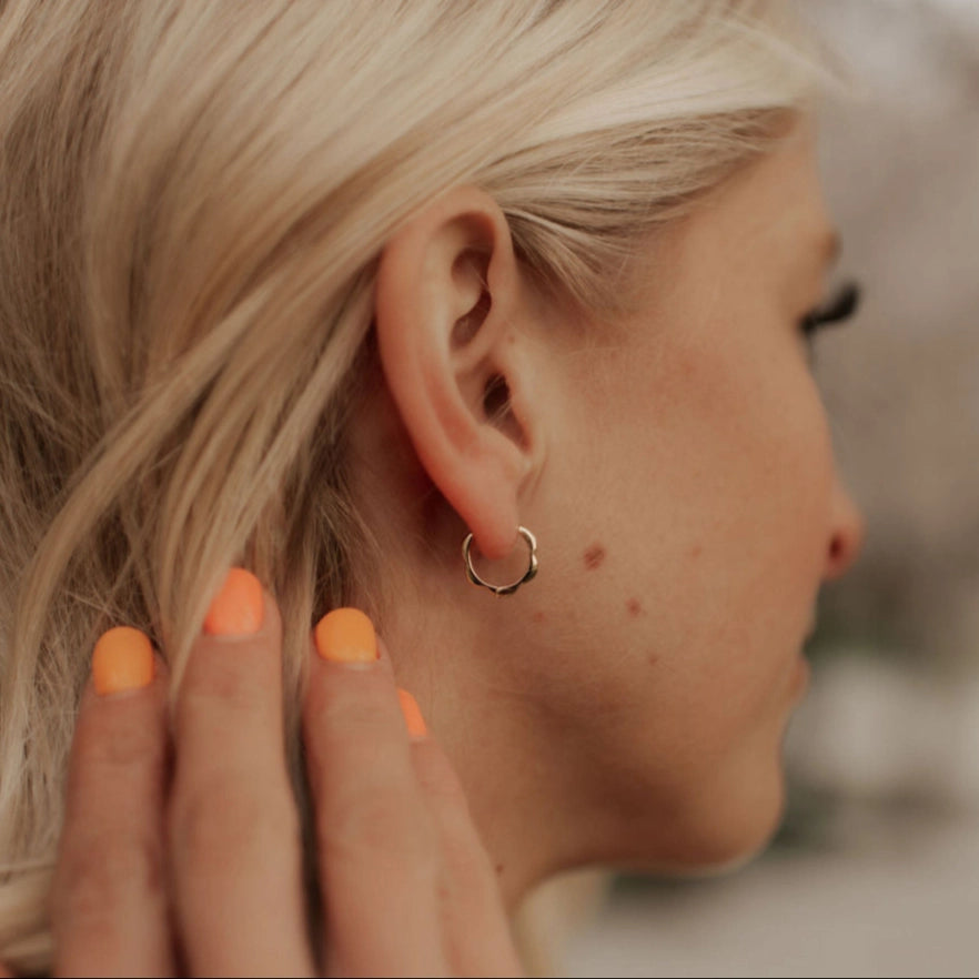 Close-up of a person wearing a small floral hoop earring with a blurred background