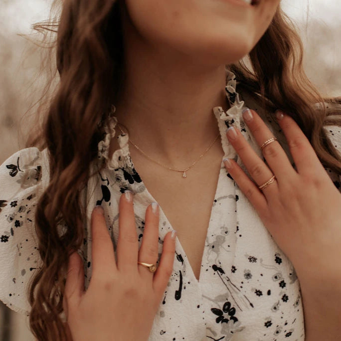 Close-up of a person wearing a floral dress with a necklace and rings.