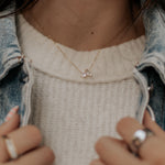 Load image into Gallery viewer, Person wearing a necklace with a small pendant, holding a phone, and wearing rings.
