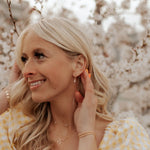 Woman adjusting an earring with a blurred floral background