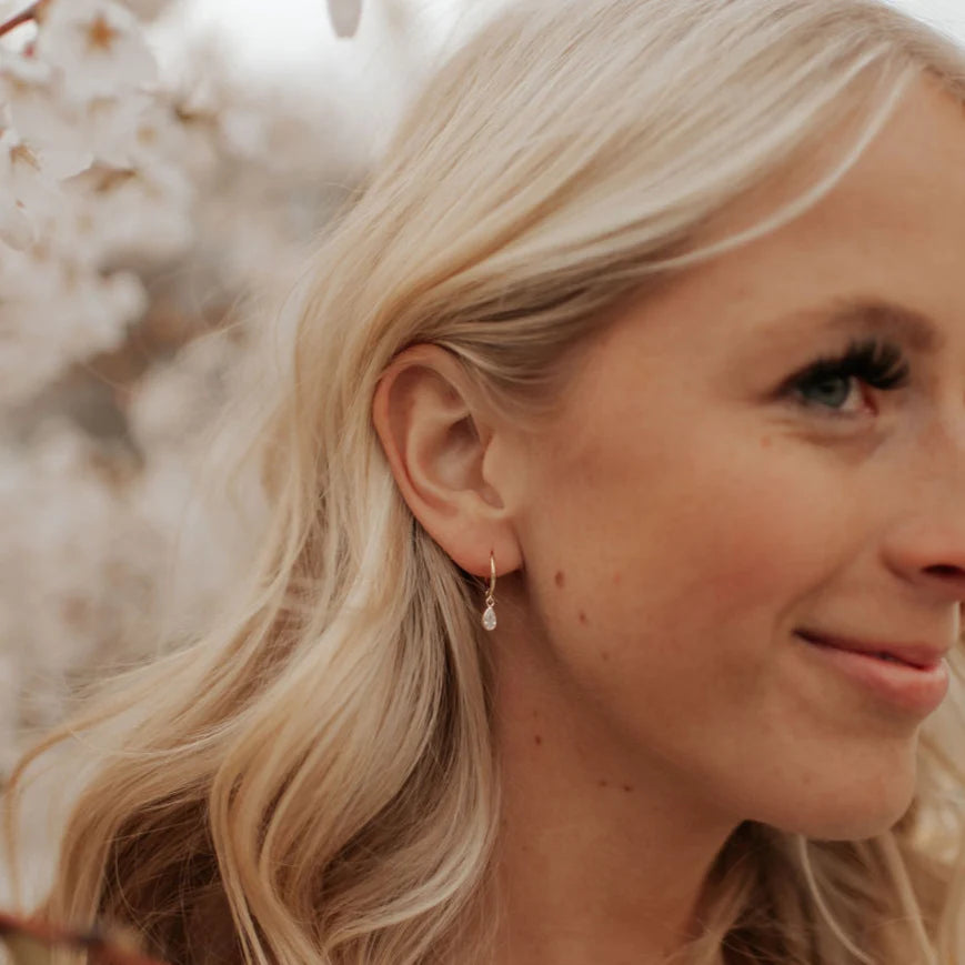 Close-up of a woman with blonde hair and earrings, with a blurred natural background